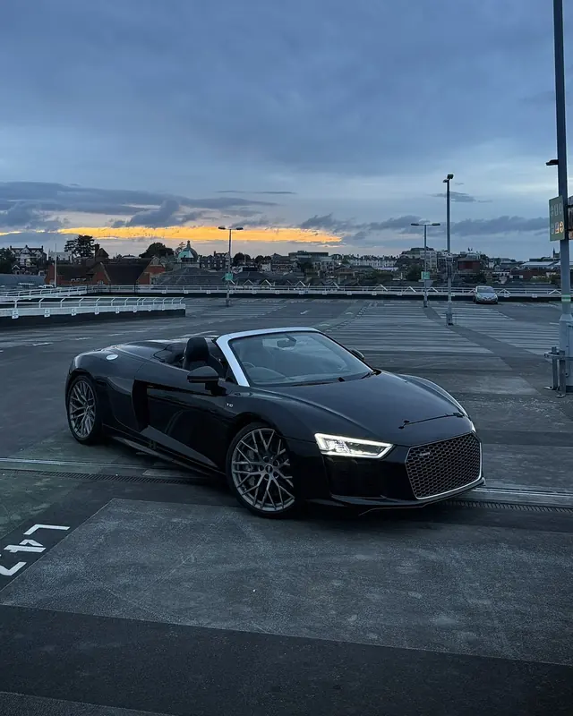 Harry's black Audi R8 on a rooftop car park at sunset.